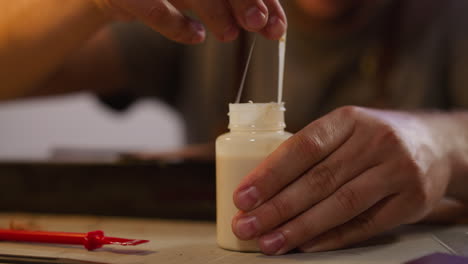 Craftsman-takes-away-dry-parts-of-glue-from-bottle-at-table