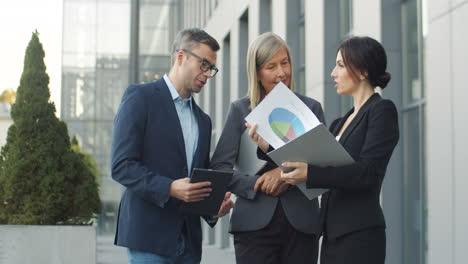 businessman and female colleagues with documents and tablet device, talking and discussing about a project in the street 1