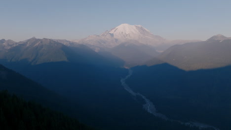 Wide-aerial-footage-of-a-valley-in-the-Cascade-Mountains-with-a-river-in-it-in-the-morning-and-Mount-Rainier-in-the-background