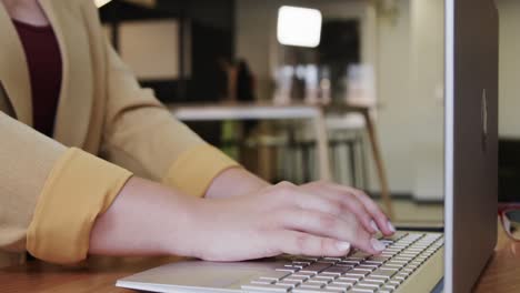 Midsection-of-plus-size-caucasian-casual-businesswoman-using-laptop-at-office-lounge