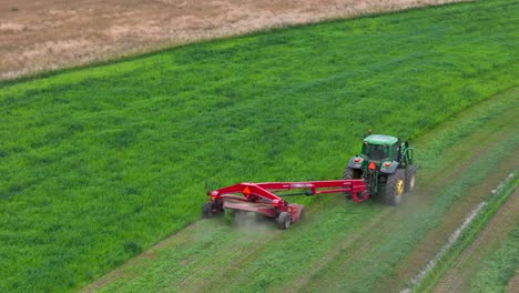 cortando las rondas: vista aérea de un tractor verde cosechando heno en la columbia británica