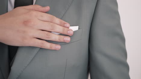 Man-adjusting-white-pocket-square-in-a-grey-suit-jacket,-emphasizing-elegance