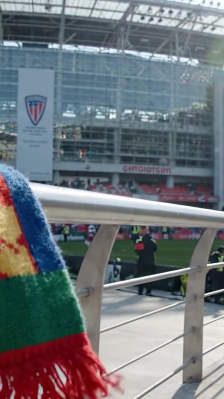 Farverigt tørklæde draperet over et gelænder med et stadion i baggrunden, der fanger stemningen af spænding og forventning før en begivenhed.