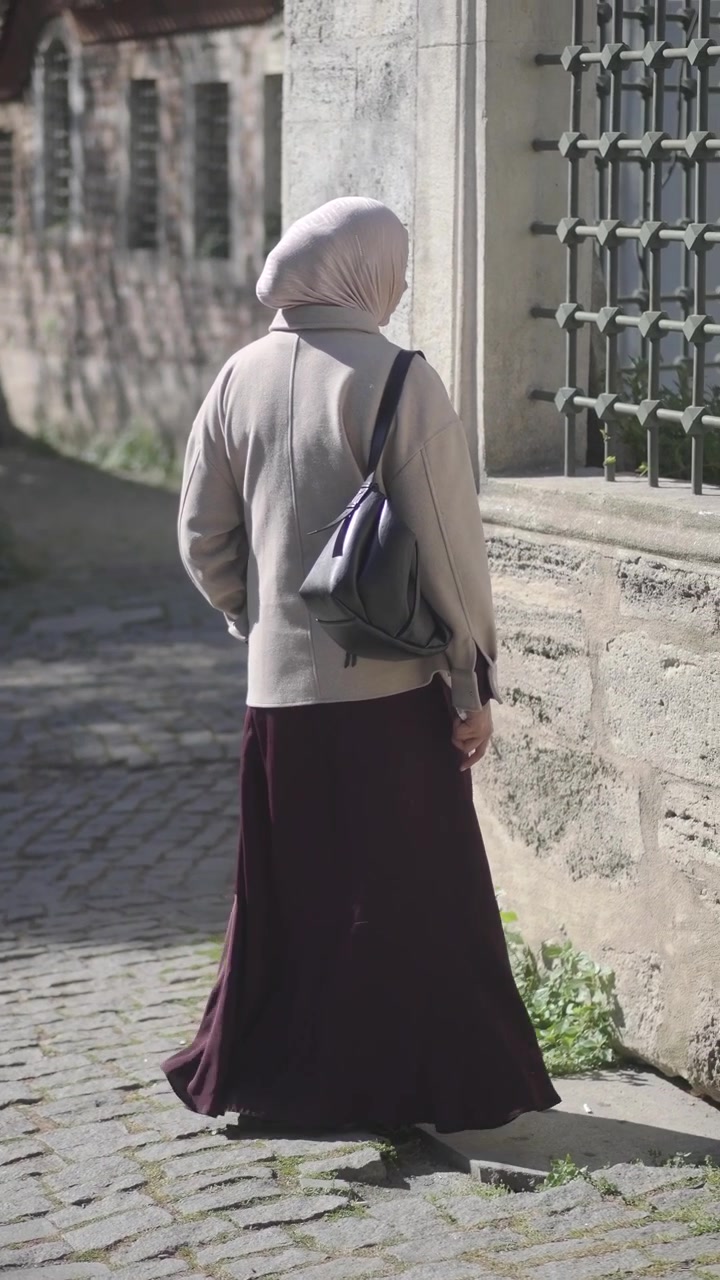 Woman in Hijab Standing by Stone Wall on Cobblestone Street