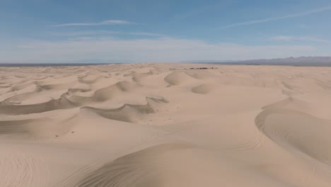 Fliegen-über-Weite-Und-Endlose-Weiten,-Luftdrohnenaufnahme-Von-Wüstensanddünen-Mit-Gipfeln-Und-Graten,-Blauer-Himmel-Darüber