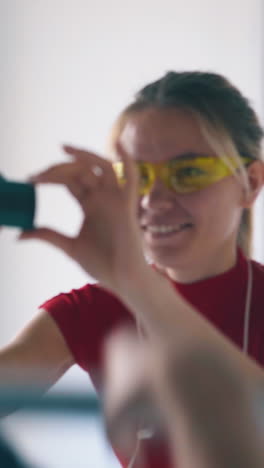 joyful young woman with yellow goggles and smartphone shoots dancing boyfriend at renewal in light spacious room