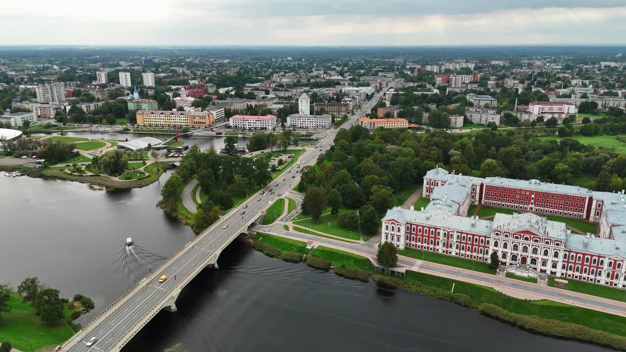 Jelgavan palatsi, joka tunnetaan Latvian Versaillesina, hohtaa Lielupe-joen rannalla, kun silta sykkii liikennettä – kuvattuna barokkiarkkitehtuurin ja joenrantakaupunkisuunnittelun yläpuolella leijuvalla drone-otoksella.