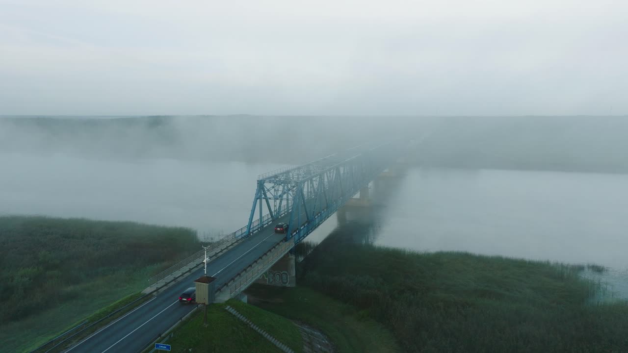⁇ 은 여름 아침에 젤루페 강을 가로지르는 철강 다리의 공중 뷰, 강 위로 떠오르는 안개, 자동차 운전, 넓은 드론  ⁇ 이 낮게 앞으로 이동