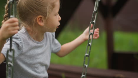 little girl plays swings with chains on ground in hotel yard