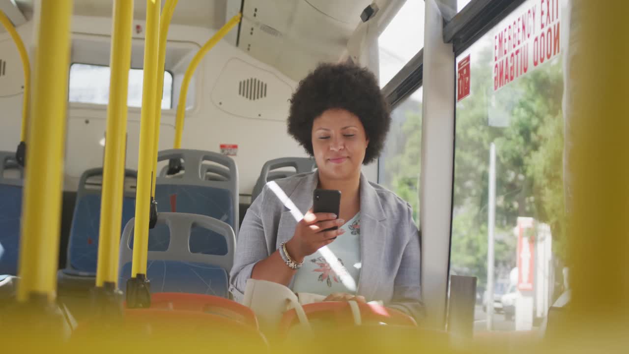 mujer biracial feliz de talla plus usando un teléfono inteligente en el autobús