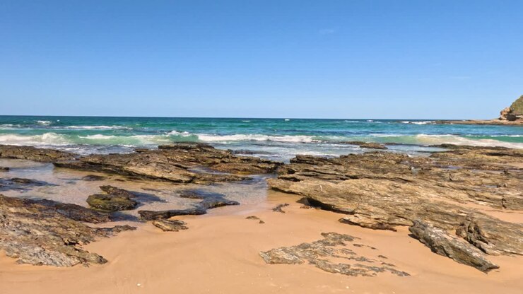 Vagues déferlantes sur une plage rocheuse sous un ciel dégagé