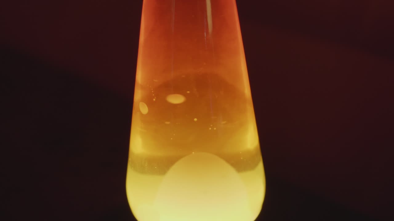 Close up of a vintage lava lamp in a warm and vintage setting. Orange lighting and bubbles create a retro atmosphere. Shot in 60 Frames for slow motion