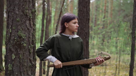 Careful-girl-with-crossbow-looks-around-walking-through-wood