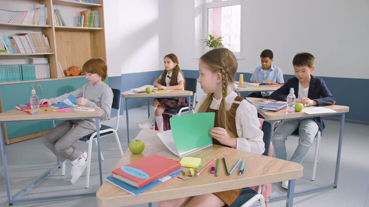 Gruppo multietnico di bambini in classe che aprono i quaderni durante la lezione di inglese