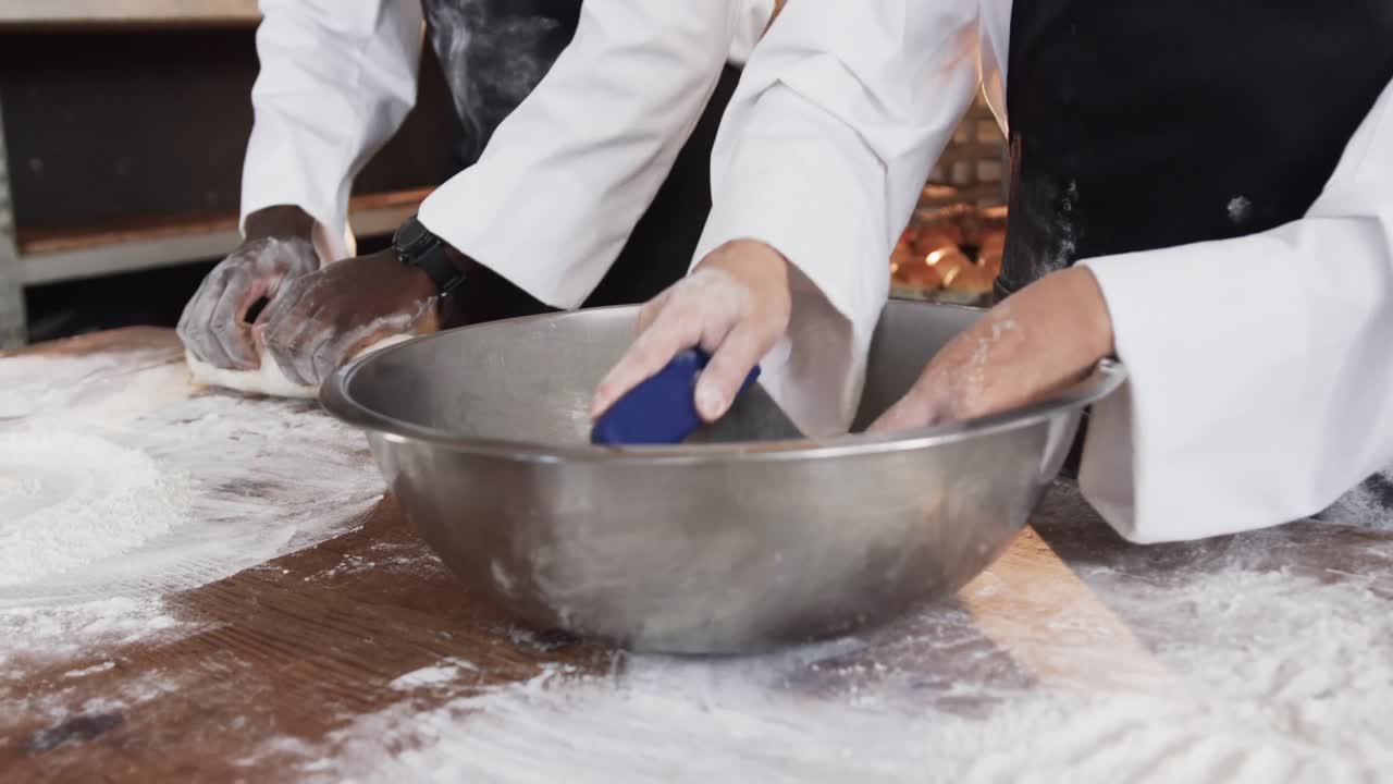 Diversi panettieri che lavorano nella cucina di una panetteria, impastando l'impasto sul bancone al rallentatore.