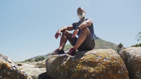 Senior-african-american-man-exercising-sitting-on-rocks-by-the-sea