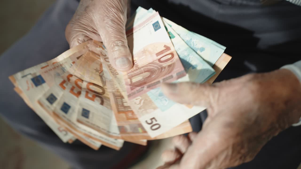pensionista en desesperación contando sus miserables ingresos de pensión, abuelo sosteniendo papel moneda de euro en sus manos arrugadas sentado en la silla. problema de la pobreza durante la inflación financiera mundial