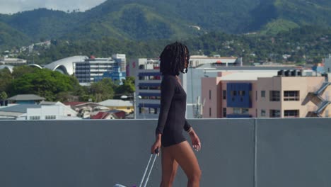 Young-in-high-heels-walking-on-a-rooftop-with-her-luggage