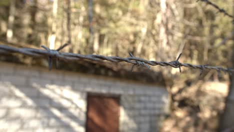 Sharp-string-of-barb-wire-front-of-a-demolished-building,-close-up-with-dolly-movement