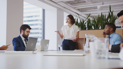 Geschäftsfrau-Hält-Präsentation-Vor-Kollegen,-Die-Im-Modernen-Büro-Am-Tisch-Sitzen