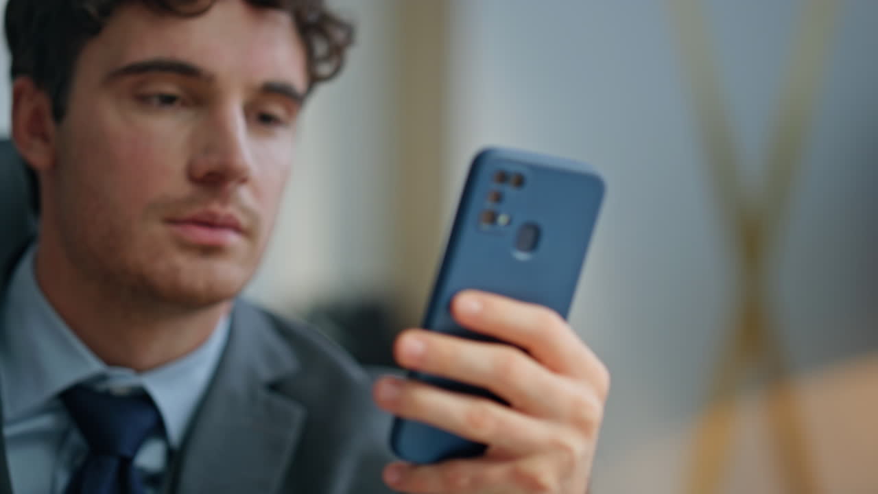 Uomo attraente che legge lo smartphone seduto alla scrivania in primo piano. CEO che naviga in internet.