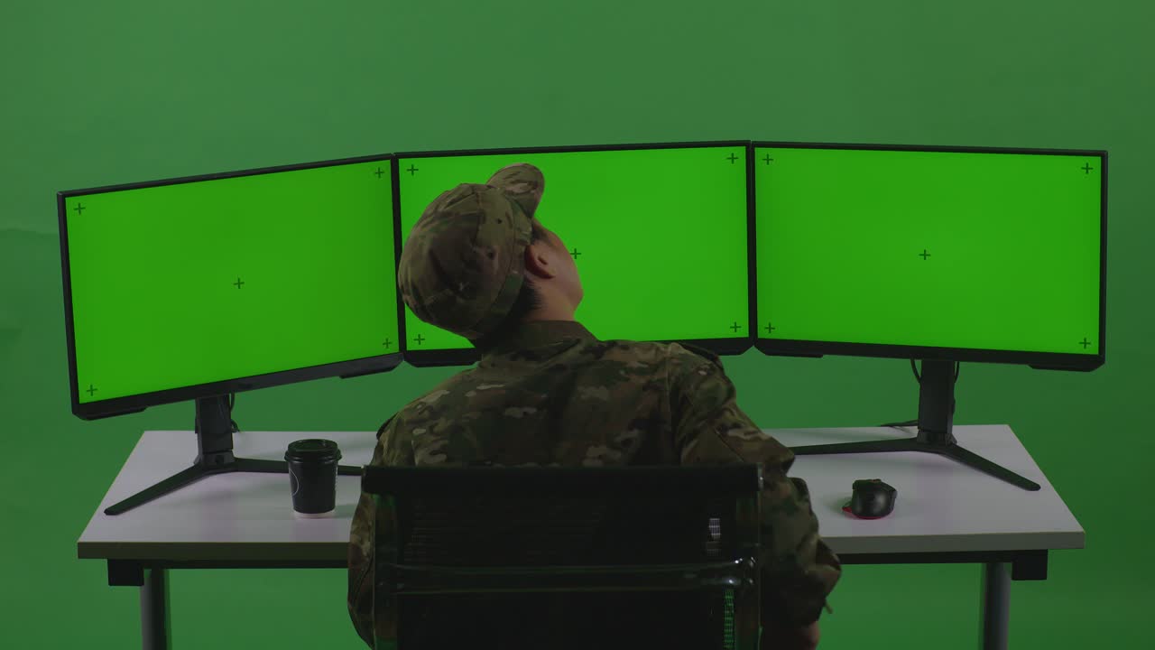 задний вид азиатского мужчины-солдата с болью в спине во время работы с макетным нескольким компьютерным монитором в студии с зеленым экраном