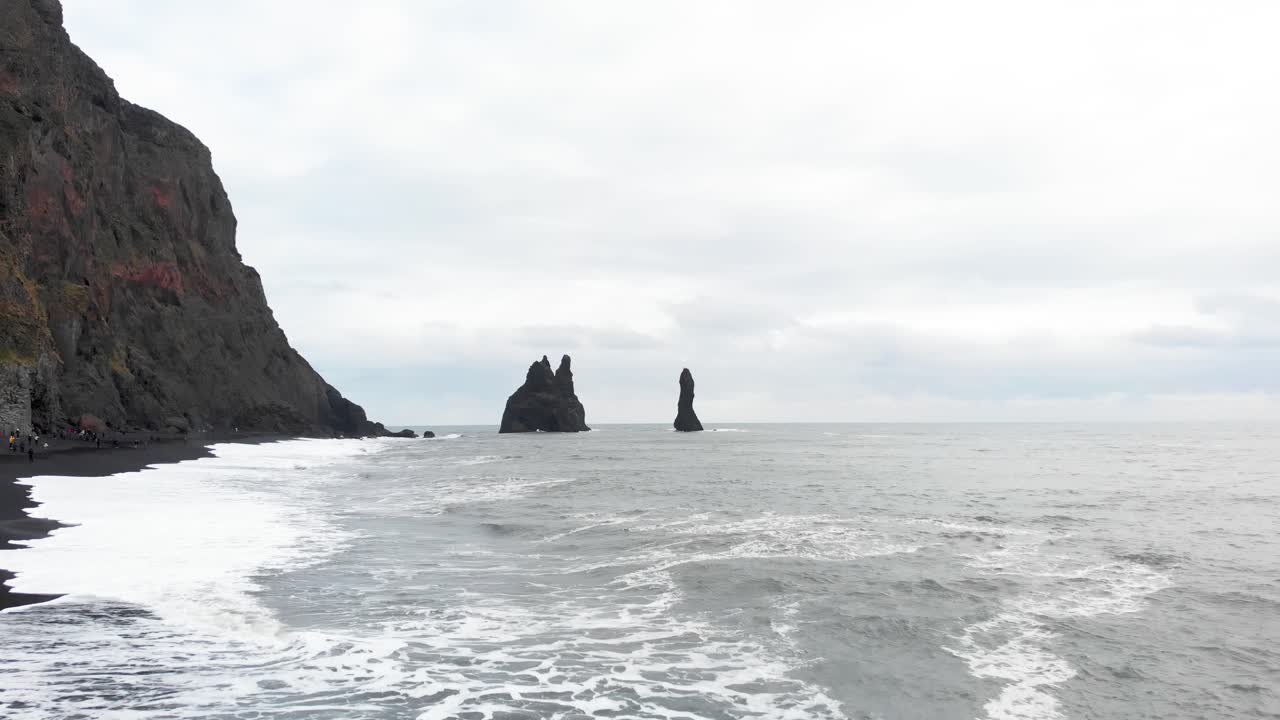 olas espumosas golpeando reynisfjara playa de arena negra, columnas de roca más allá