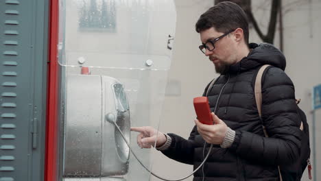 hombre usando un teléfono público en la lluvia