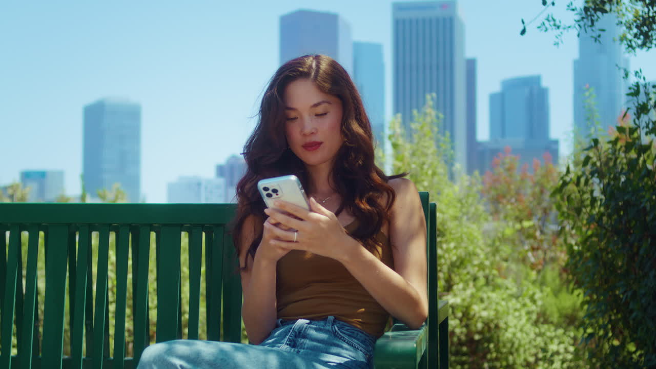 관광객이 벤치에 앉아서 전화번호를 호출합니다. 아시아 소녀가 야외에서 전화를 합니다.