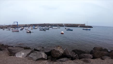 pan a la derecha con barcos atracados en un puerto con rocas negras