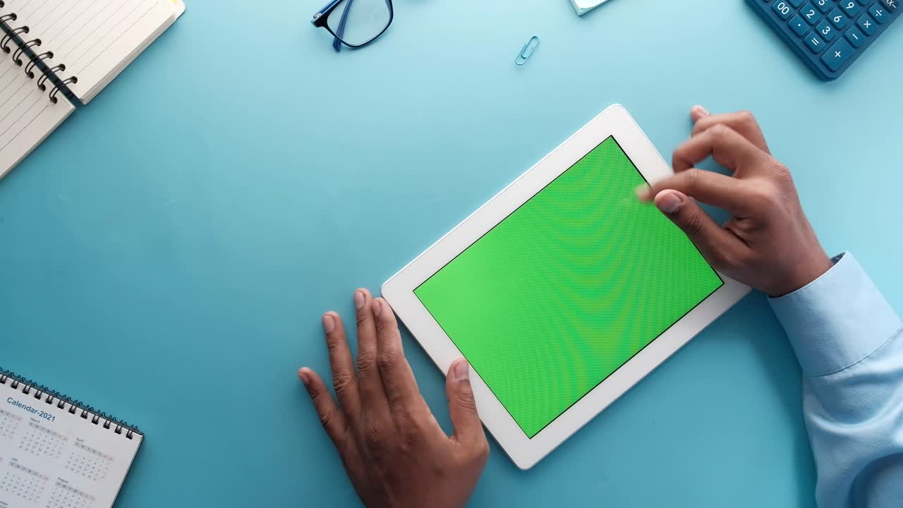 Person using a tablet with a green screen on a desk
