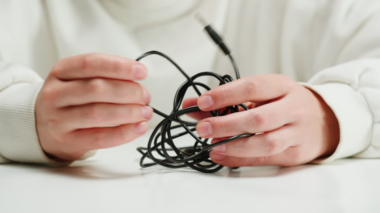 Young woman trying to untangle the black headphones close-up. Tangled wires on table. Trying to untangle many messy cables
