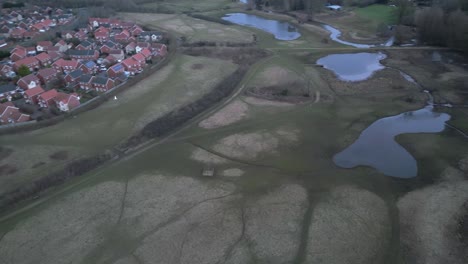 a park in norwich with winding water bodies and residential areas nearby, cloudy day, aerial view