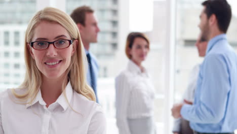 Mujer-De-Negocios-Sonriendo-A-La-Cámara-Con-Colegas-Detrás-De-Ella