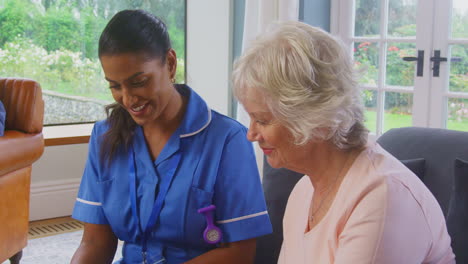 Senior-Couple-At-Home-With-Woman-Talking-To-Female-Nurse-Or-Care-Worker-Using-Digital-Tablet