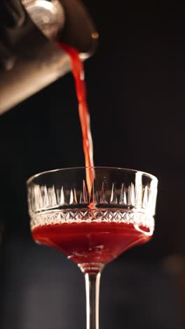 pouring a red cocktail into a martini glass