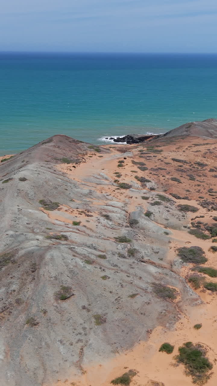 Splendido video verticale con drone su Cabo de la Vela, La Guajira, Colombia, che rivela drammatiche colline desertiche, mare turchese e sabbia arancione vibrante sotto la luminosa luce naturale del giorno. Ideale per i social media