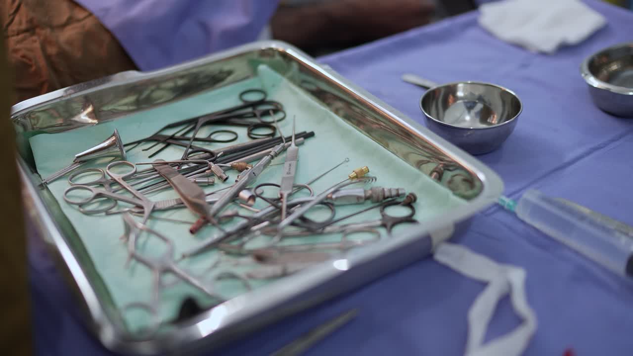Instrumentos cirúrgicos estéreis dispostos em uma bandeja de metal em uma sala de cirurgia, preparados para um procedimento médico em uma mesa coberta