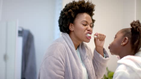 young african american mother brushes her teeth at home, with daughter