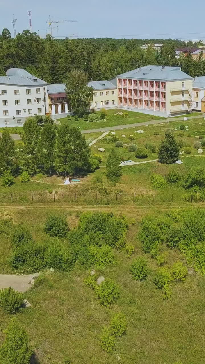 modern dwelling buildings and distant couple in beautiful park on green hill on nice autumn day aerial view