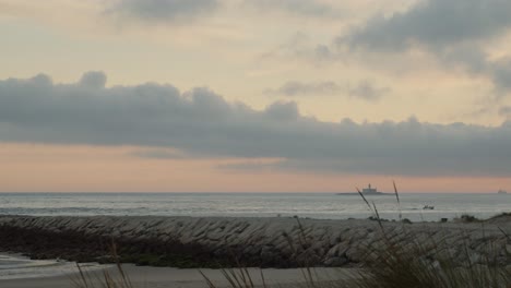 Fishing-boat-returning-to-coast-in-the-golden-hour-with-lighthouse-on-the-background-at-Costa-da-Caparica