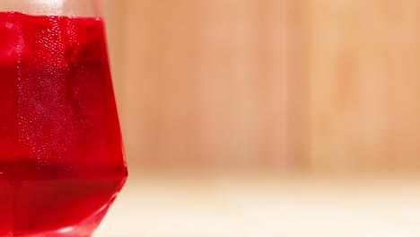 a vibrant red drink fills a glass against a blurred wooden background, showcasing its rich color and texture.