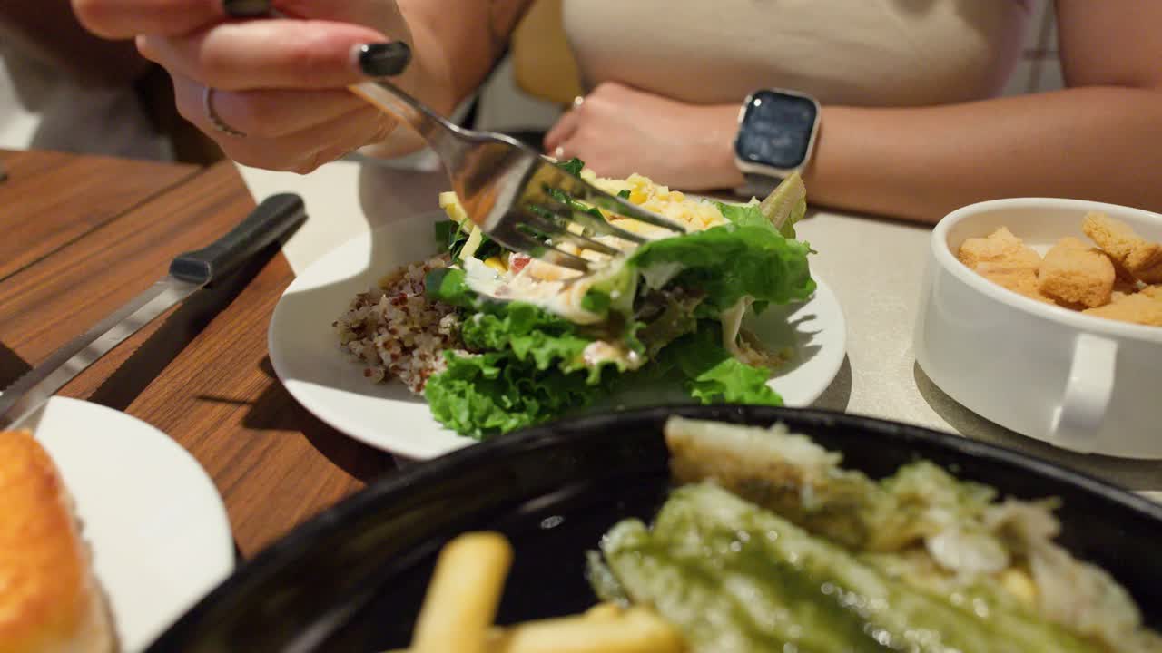 Close-up of woman mixing and eating quinoa salad with creamy dressing in warm restaurant lighting