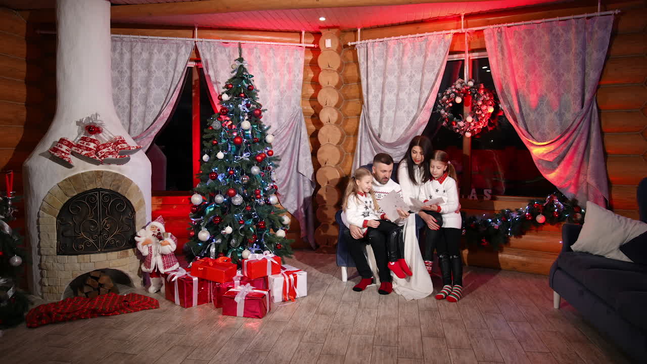 Family sit together in Christmas decorated living-room. Parents have pleasant conversation with their lovely daughters. Cozy atmosphere at home at winter holidays.