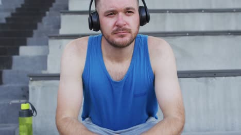 caucasian male athlete sitting, wearing headphones and listening to music