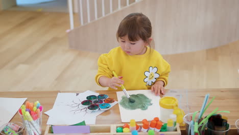 adorable little girl preschooler enjoys painting process, dipping paintbrush into watercolor paint, drawing on paper