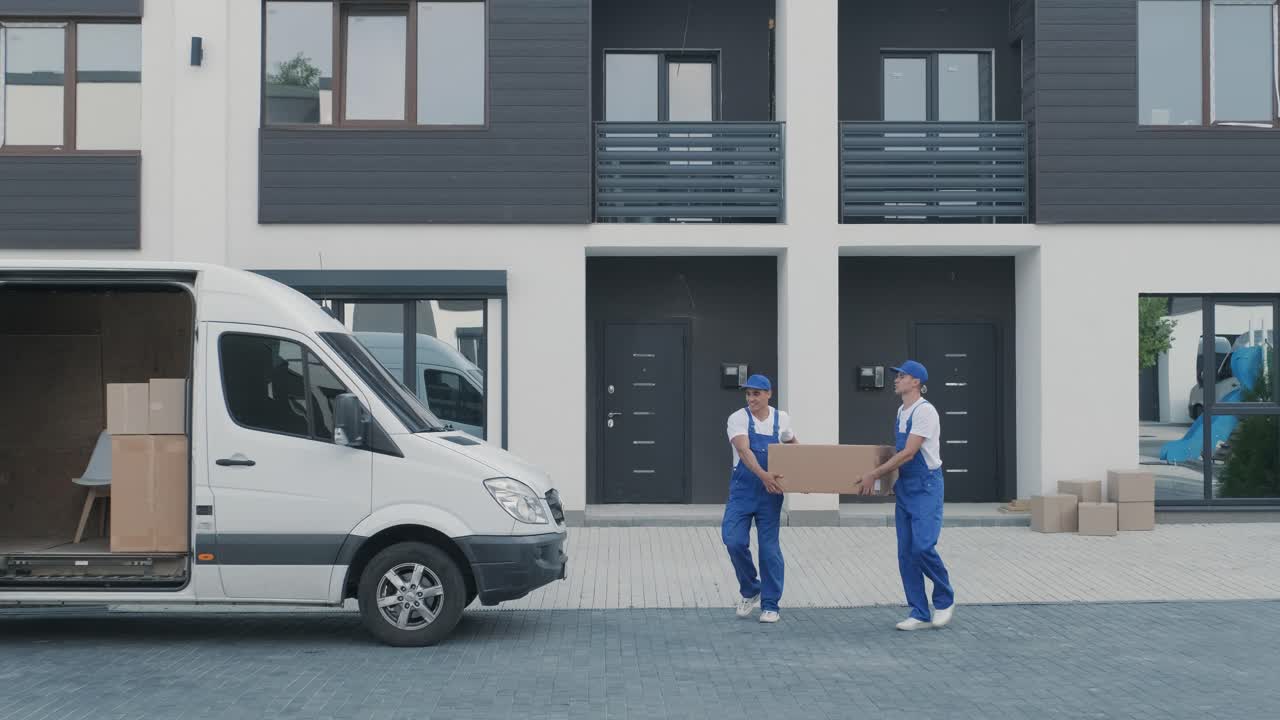 Two young workers of removal company are loading boxes and furniture into a minibus