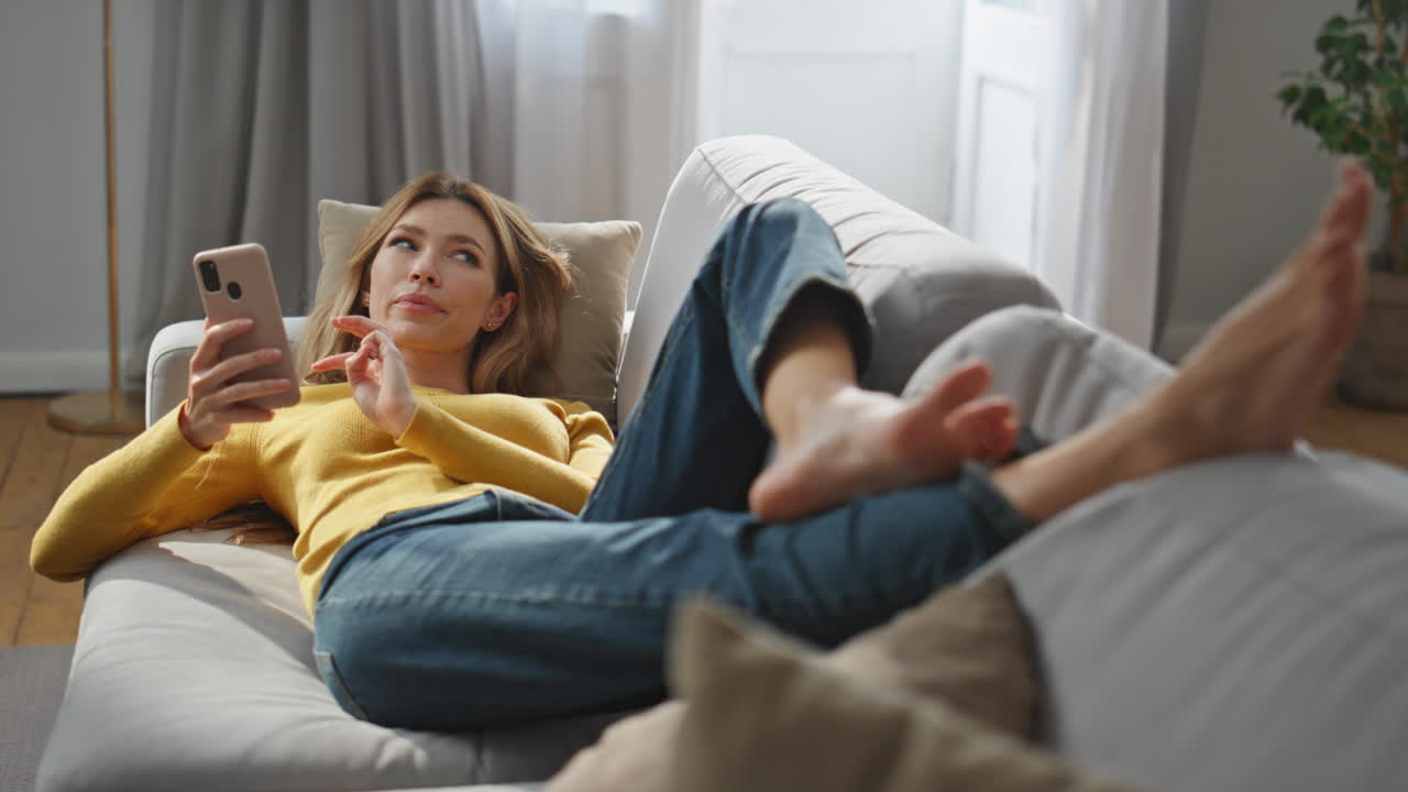 Relaxed woman creating message laying sofa living room. Pondering woman chatting