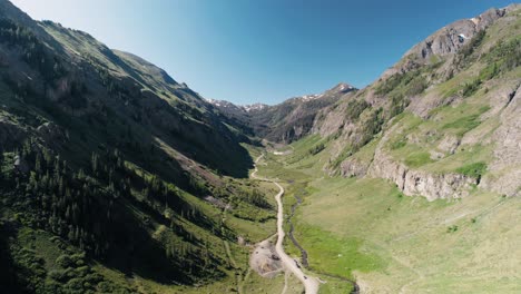 push in aerial shot in a valley of the san juan mountain range following a road and river.