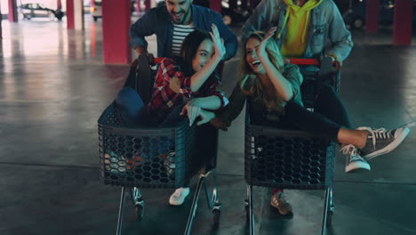 close-up view of young and happy caucasian girls sitting in trolleys, laughing and being carried by their boyfriends in the empty parking